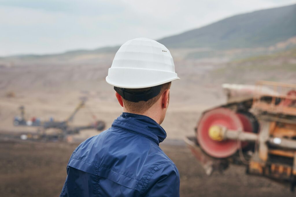 Coal mining in surface mine. Miner looking on the huge excavator.